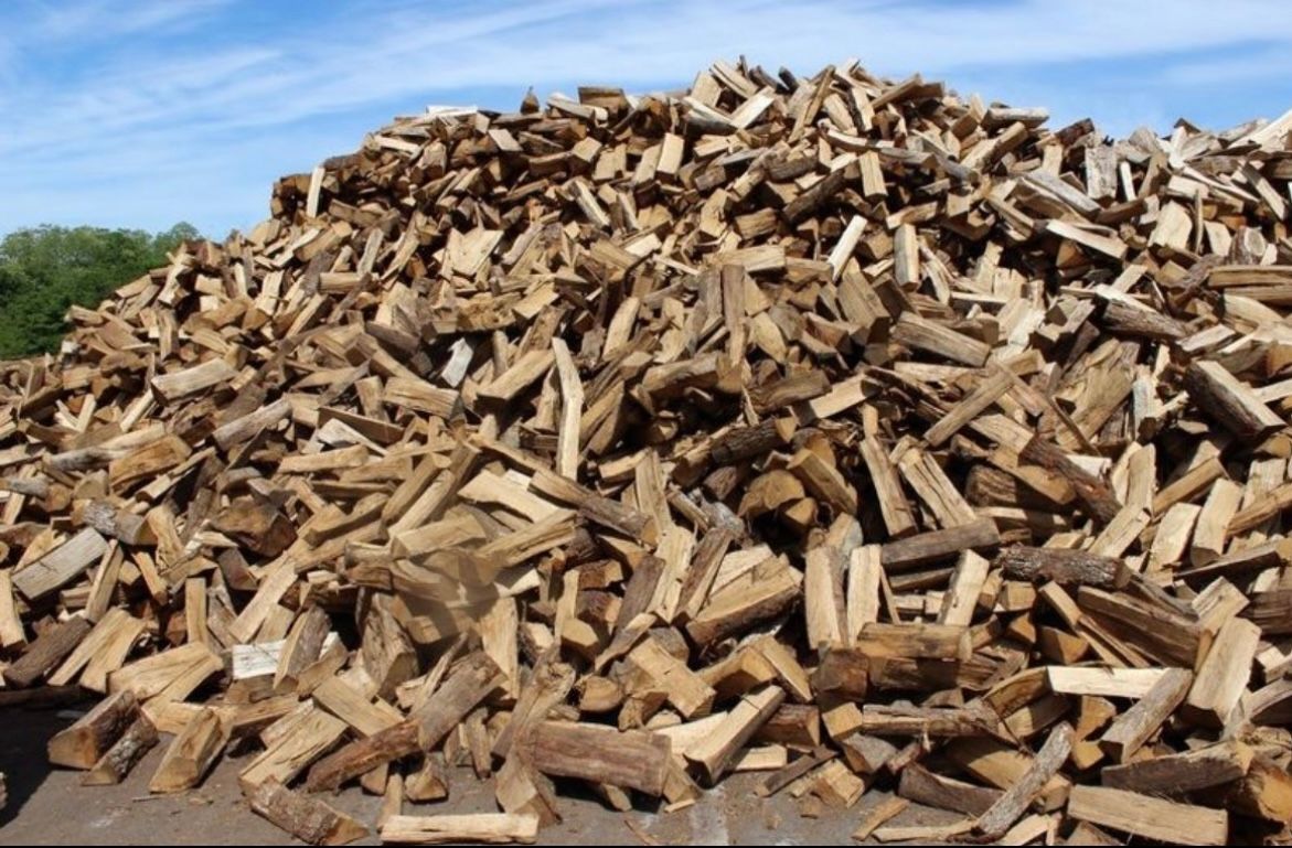 Un grand tas de bois de chauffage fendu, brun doré, empilé serré à l'extérieur.