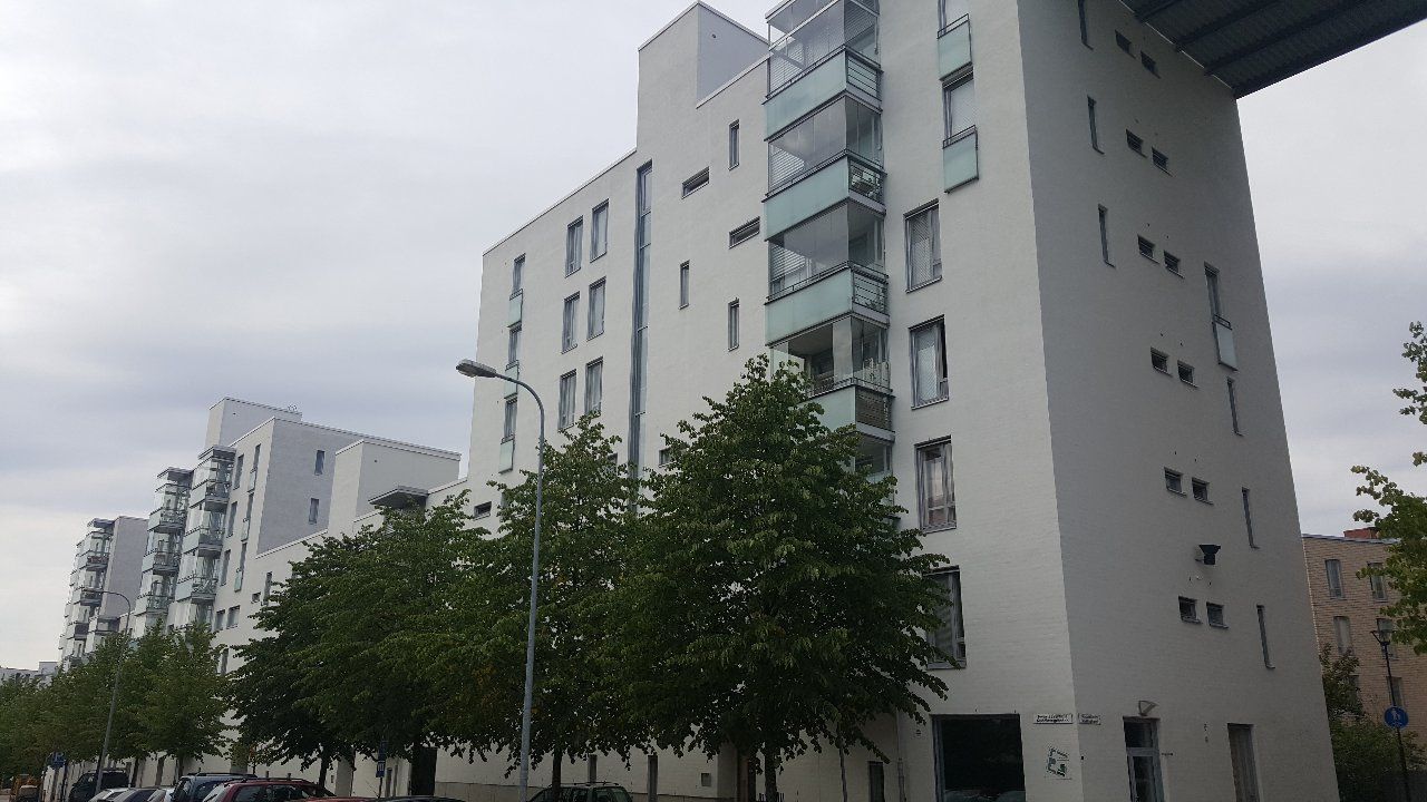 Valkoisia kerrostaloja lasiparvekkeineen ja puita pilvisen taivaan alla.