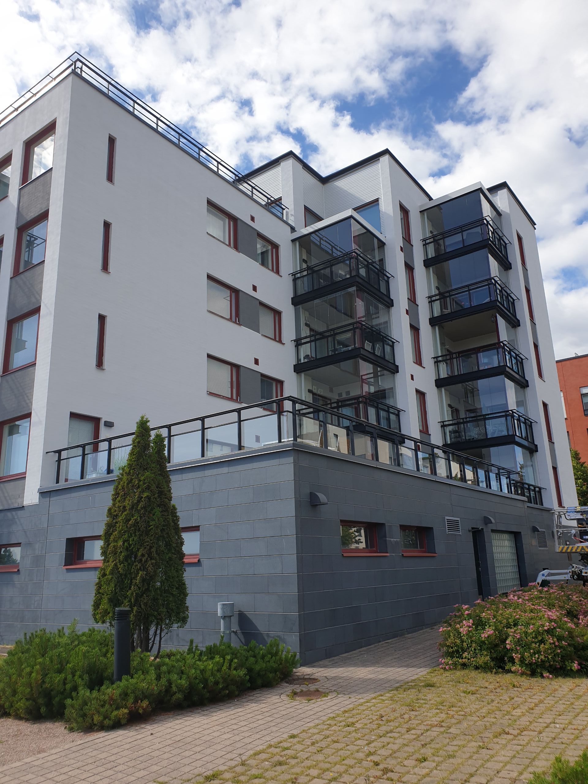 Moderni kerrostalo parvekkeineen, harmaavalkoisine julkisivuineen ja ympäröivine vehreyksineen.