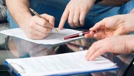 Un hombre está escribiendo en un trozo de papel mientras otra persona lo señala.