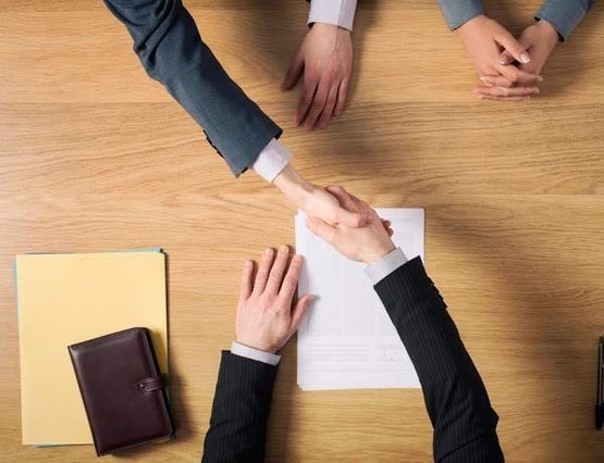 Dos personas se dan la mano por un trozo de papel sobre una mesa de madera.