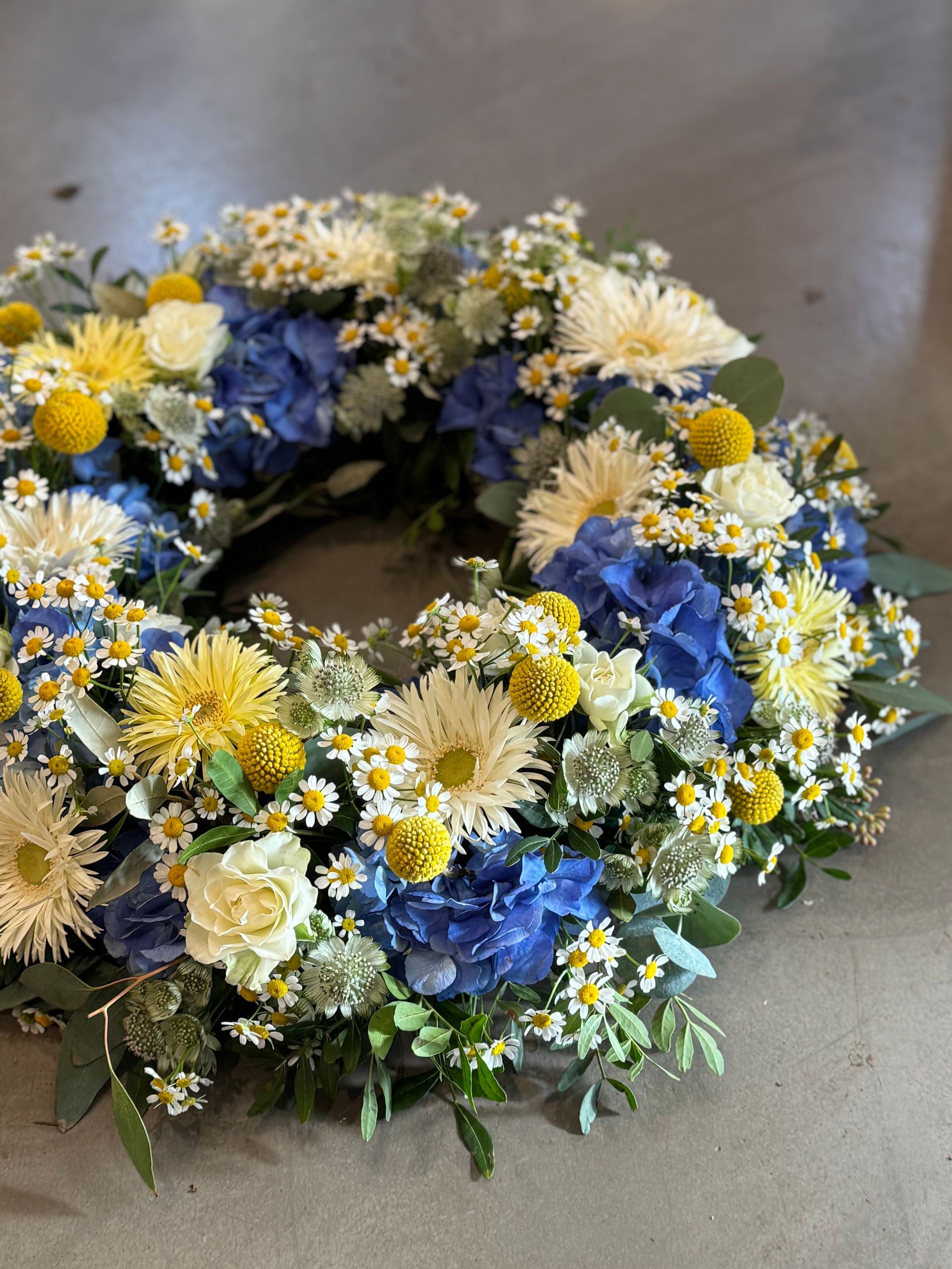 Kranz in Blau Gelb mit Rosen und Margeriten, farbenfroher Abschied