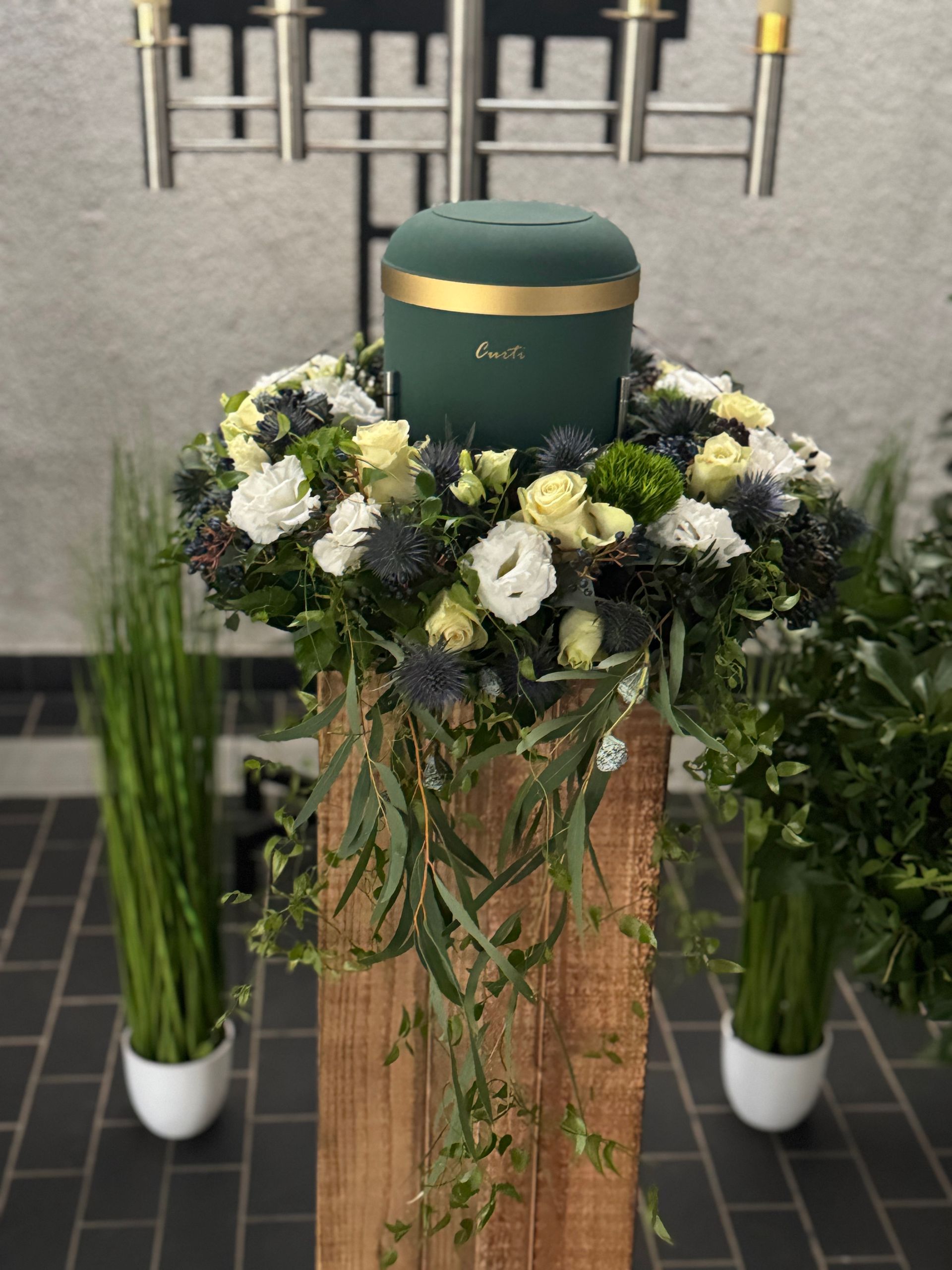 Urnenschmuck mit weißen Blumen und grünem Kranz, dezente Trauerfloristik