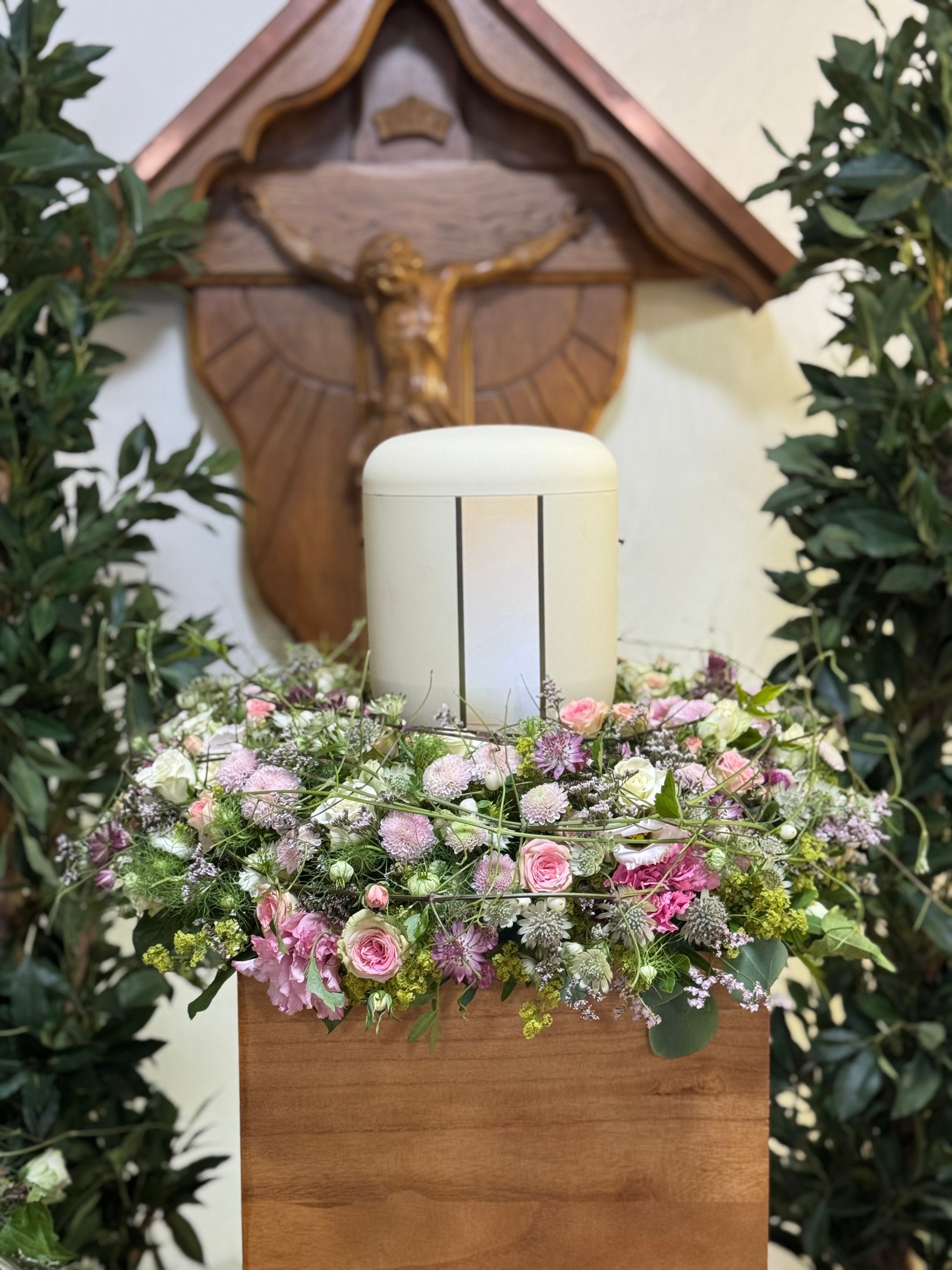 Urne mit Kreuz und Trauerfloristik im Kapellenraum eines Friedhofs als würdiger Abschied