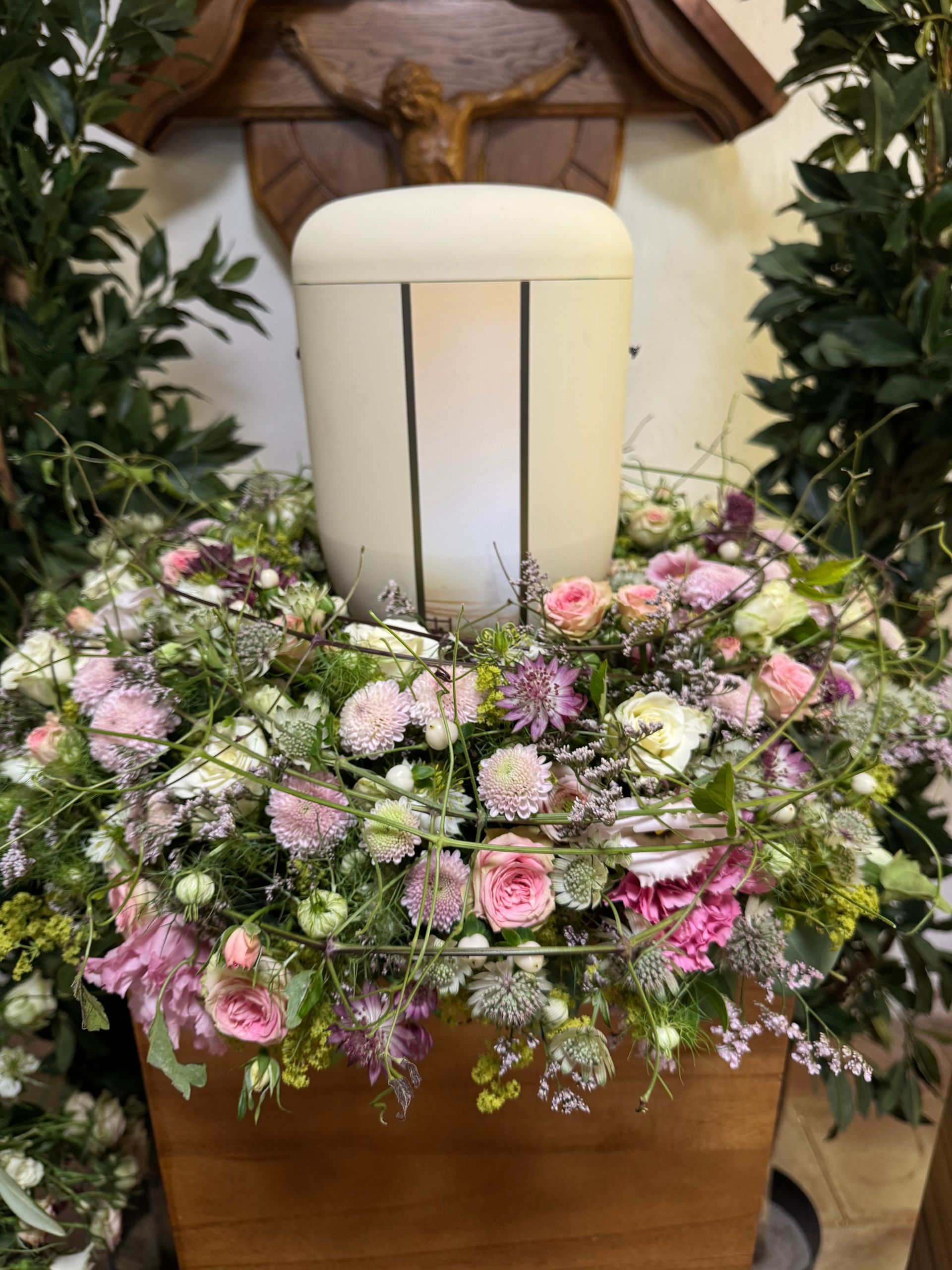 Urnenschmuck mit Kreuz im Hintergrund, stilvolle Trauerdekoration