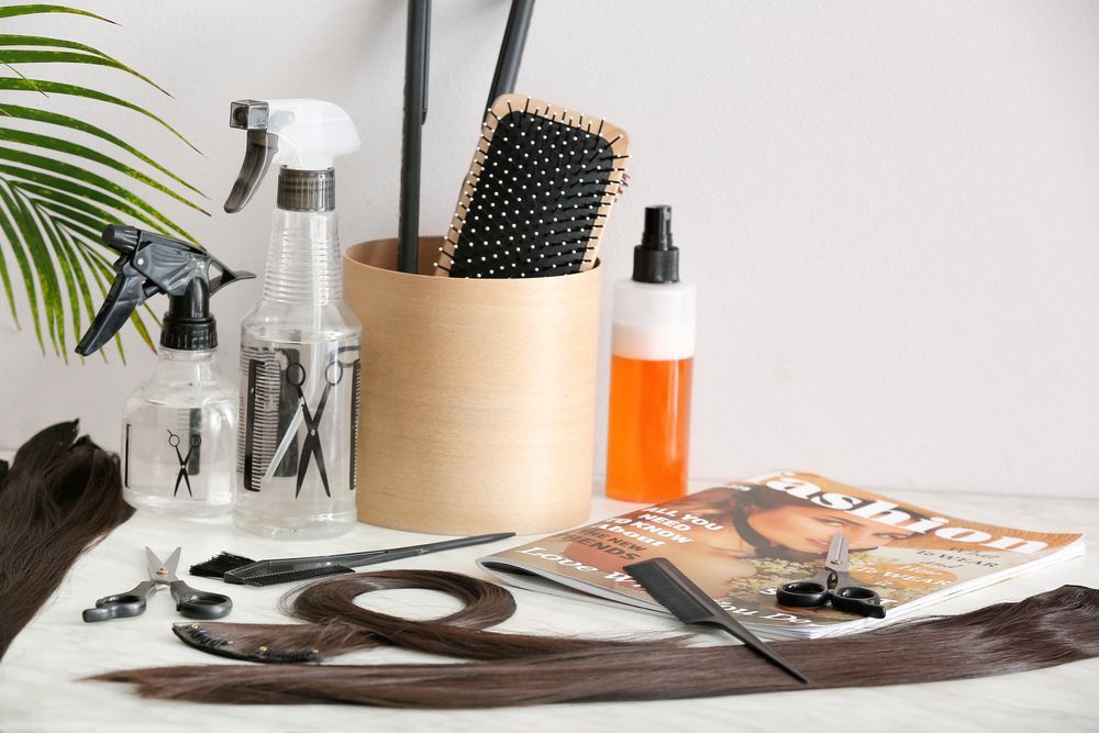 Una mesa cubierta con extensiones de cabello, cepillos, botellas de spray, tijeras y una revista.