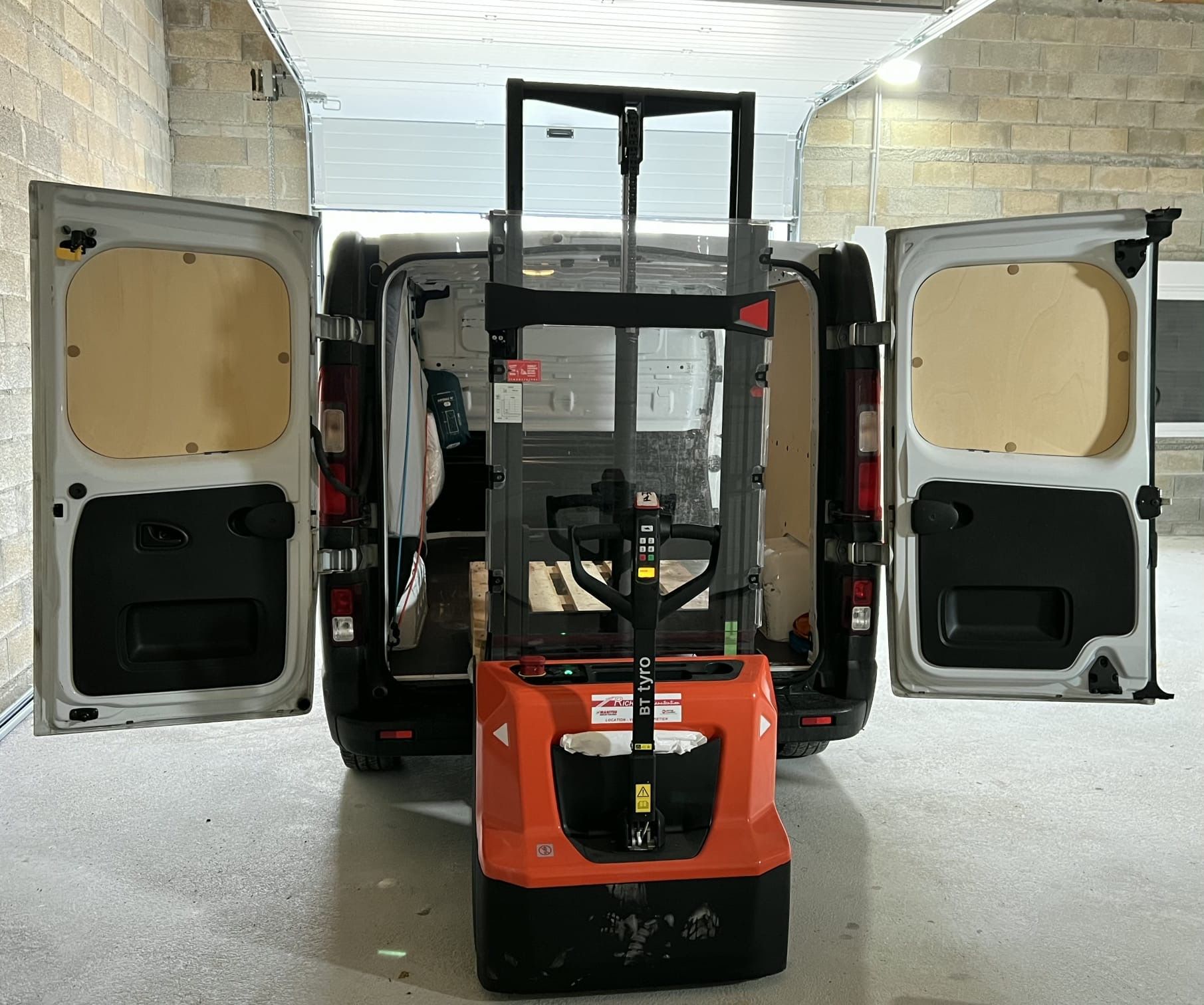 Un chariot élévateur orange se trouve à l'intérieur d'une camionnette blanche aux portes ouvertes.