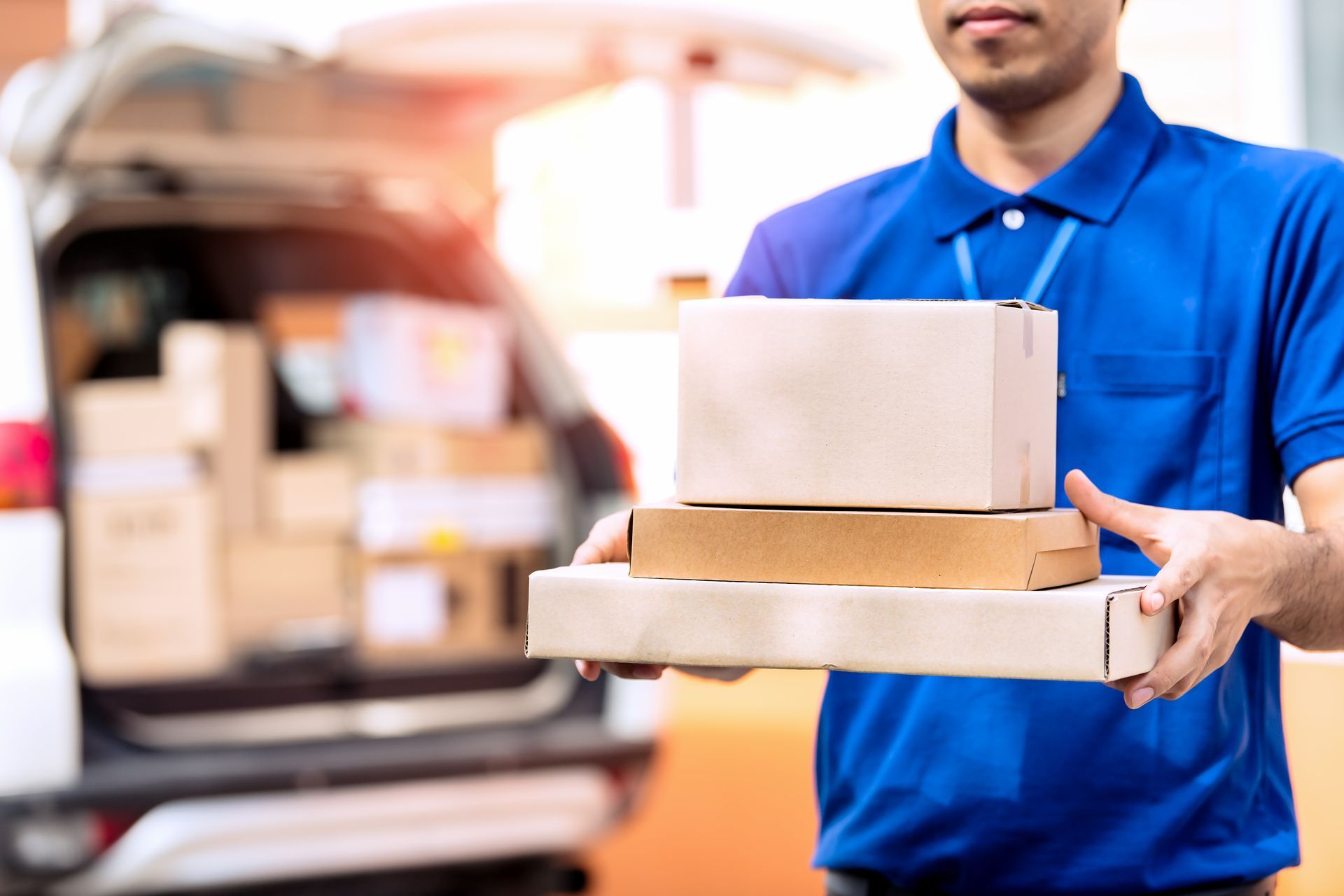 Un livreur tenant des colis près d'un véhicule rempli de cartons.