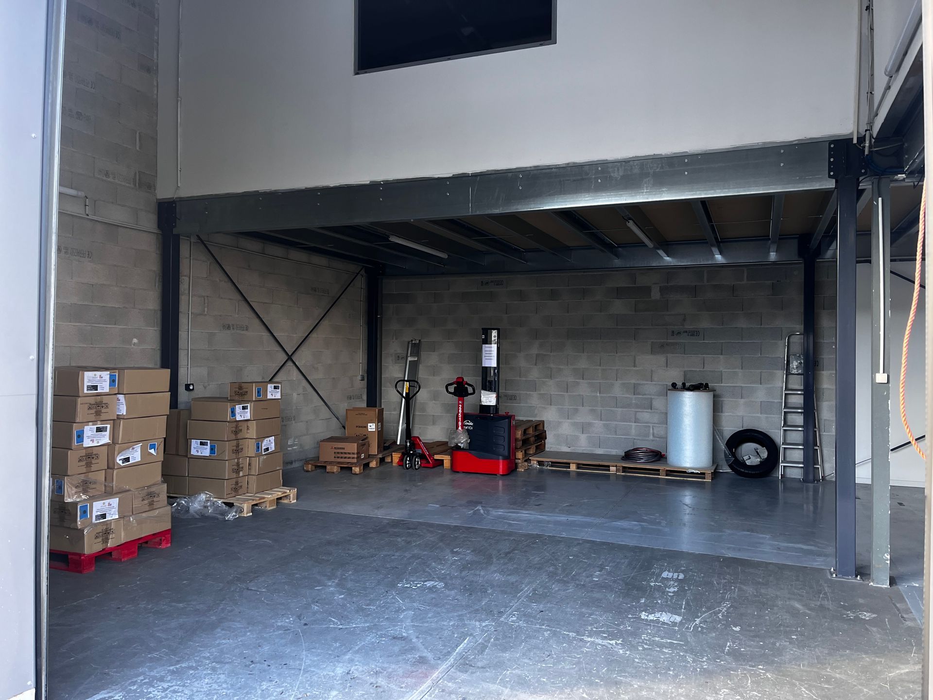 Intérieur d'entrepôt avec colis, transpalette et mezzanine.