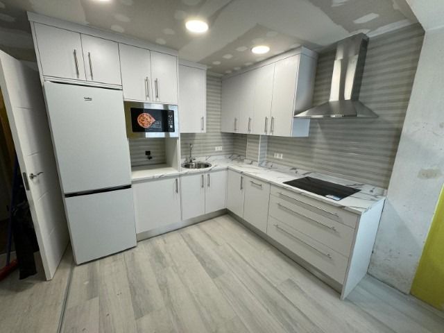 Una cocina con gabinetes blancos, un refrigerador, una estufa y un microondas.