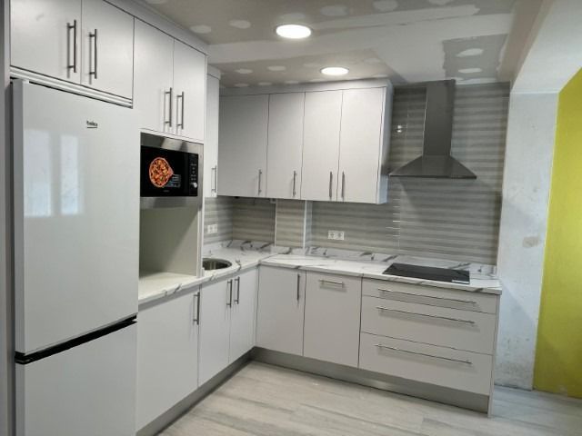 Una cocina con gabinetes blancos, una estufa, un refrigerador y un microondas.