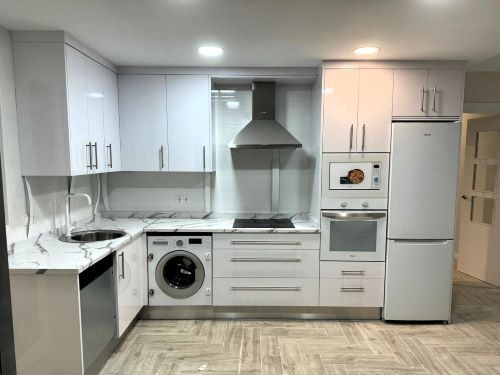 Una cocina con gabinetes blancos, lavadora y secadora, un refrigerador y un fregadero.