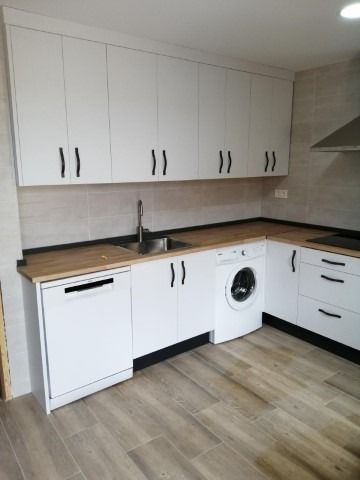 Una cocina con gabinetes blancos, una lavadora, un fregadero y un lavavajillas.