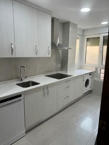 Una cocina con gabinetes blancos, un fregadero, una lavadora y secadora, y una ventana.