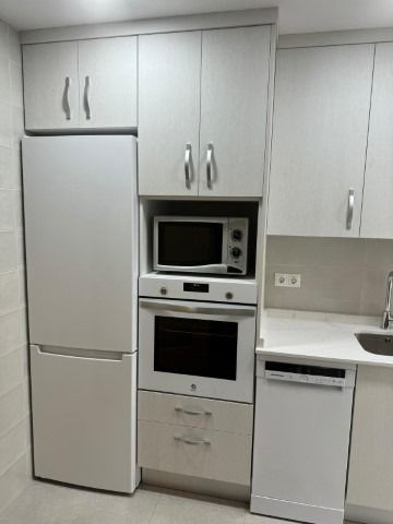 Una cocina con gabinetes blancos, un refrigerador, un horno microondas y un fregadero.