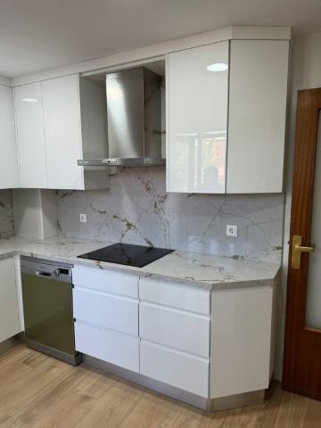 Una cocina con gabinetes blancos, una estufa y un lavavajillas.