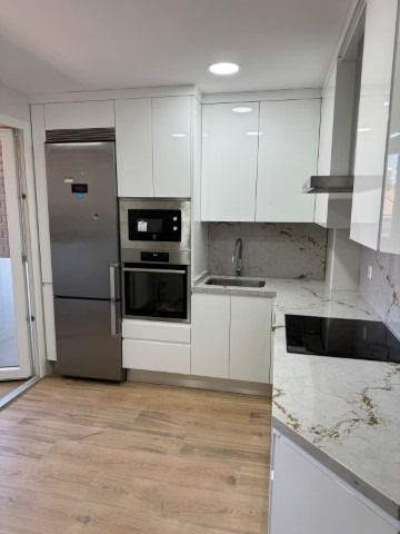 Una cocina con gabinetes blancos, electrodomésticos de acero inoxidable, un fregadero y un refrigerador.