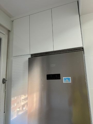 Un refrigerador de acero inoxidable en una cocina con gabinetes blancos encima.