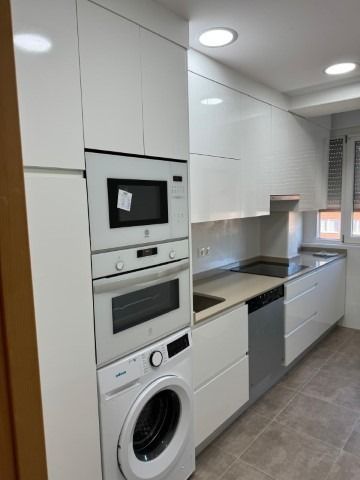 Una cocina con gabinetes blancos, lavadora y secadora y un microondas.