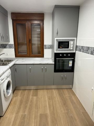 Una cocina con gabinetes grises, lavadora y secadora, un microondas y una ventana.