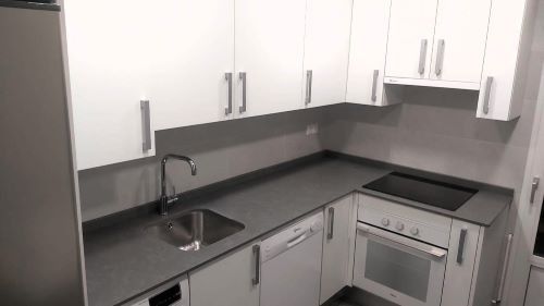 Una cocina con gabinetes blancos, un fregadero, una estufa y un refrigerador.