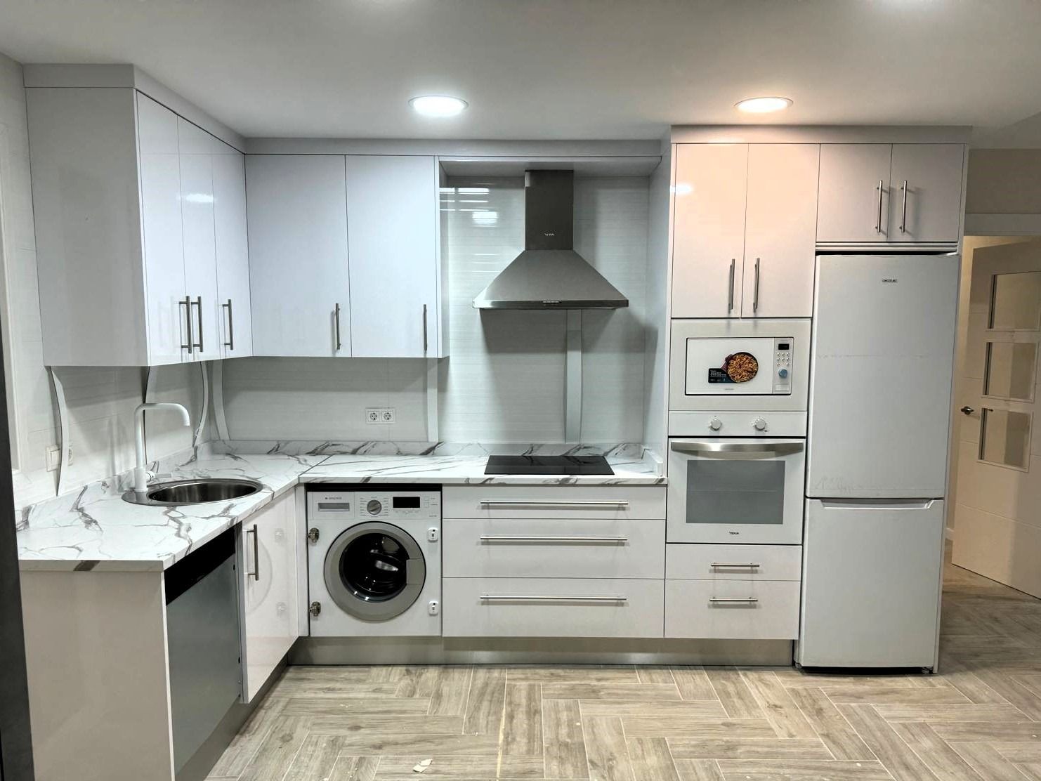 Una cocina con gabinetes blancos y electrodomésticos que incluyen lavadora y secadora.