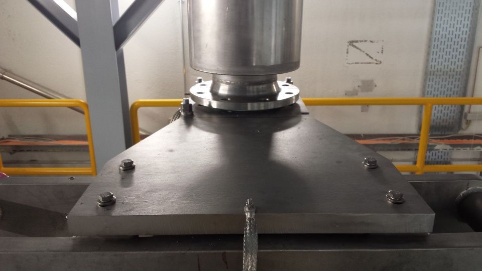 Trémie en acier inoxydable sur une plate-forme métallique avec connexions boulonnées, environnement industriel.