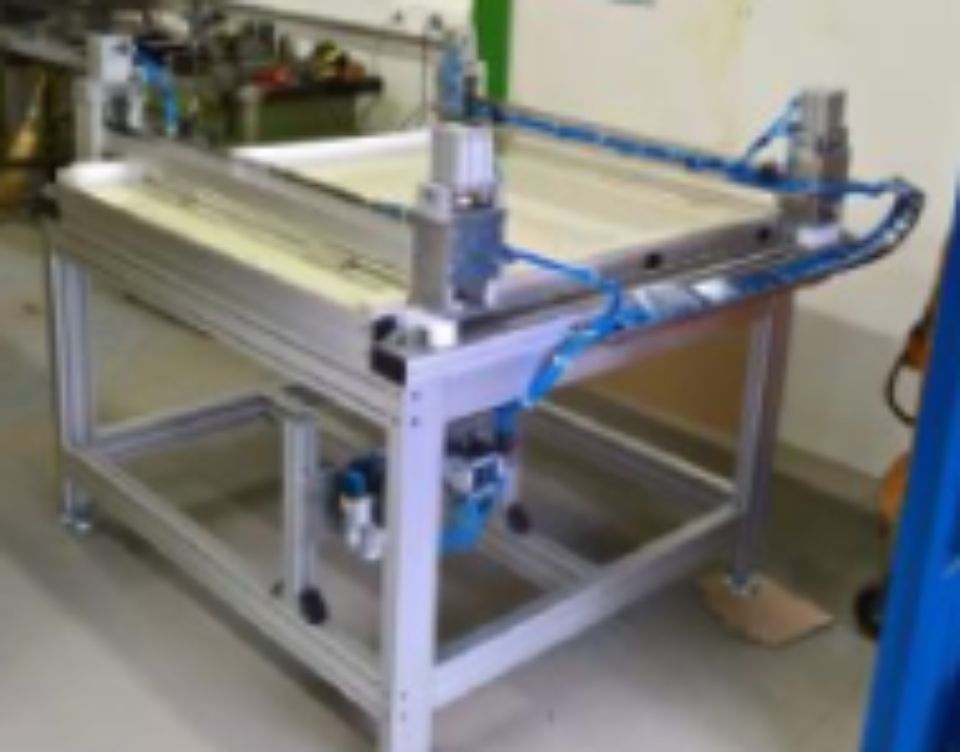 Table de travail en métal avec vérins pneumatiques et tuyaux d'air bleus; environnement industriel.