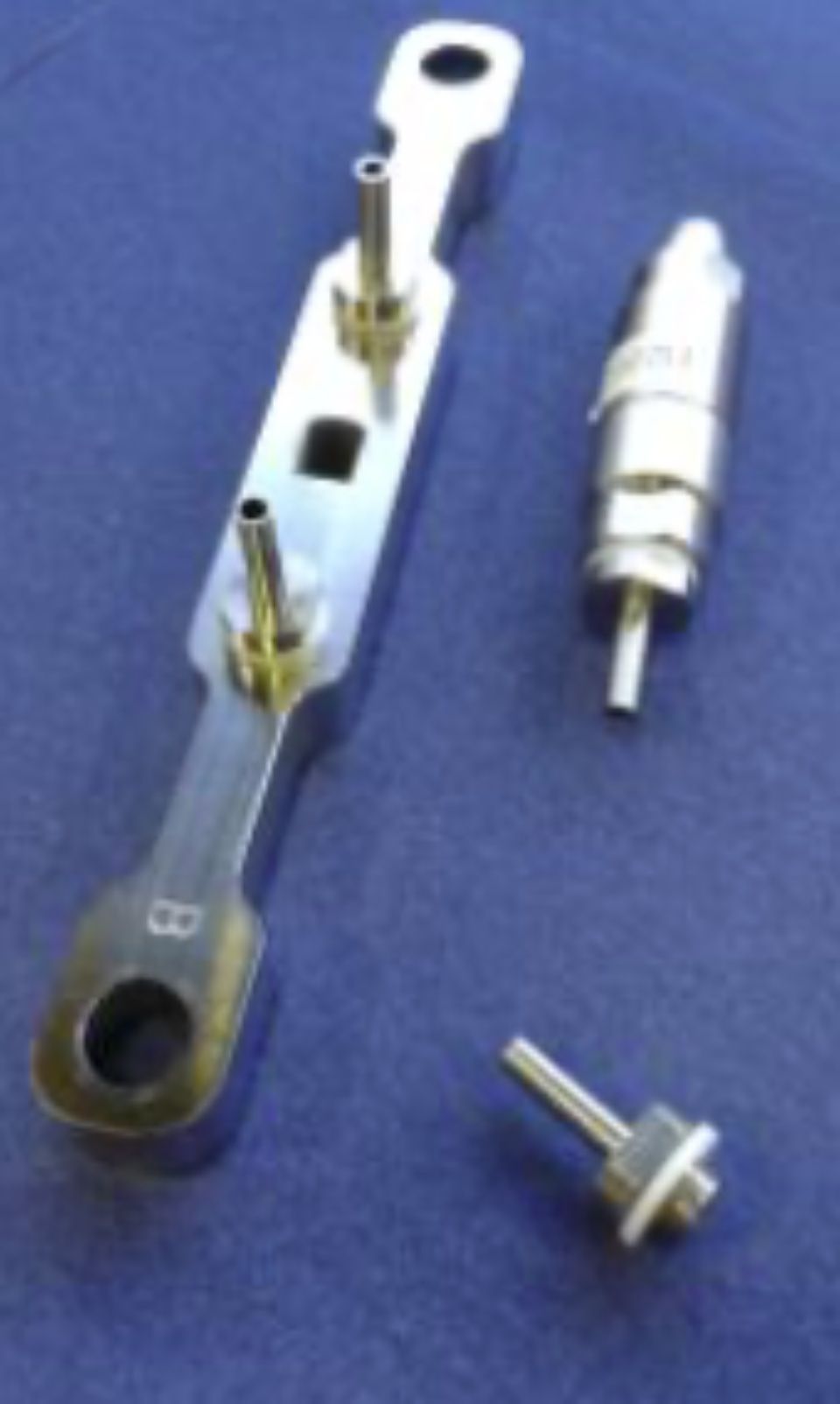 Trois instruments médicaux en métal sur une surface bleue : une barre longue et étroite avec des tubes