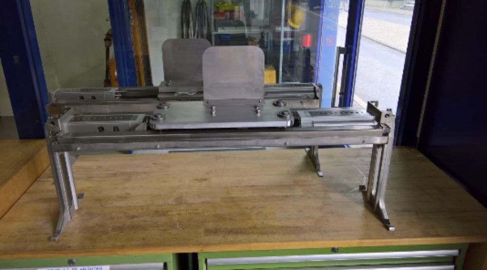 Outil de fabrication de métal sur un établi en bois, doté de bras réglables et d'une plaque centrale.