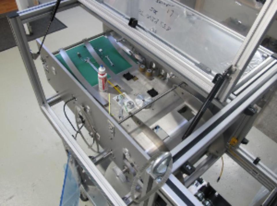 Une machine industrielle avec un tapis roulant, des outils et une enceinte de sécurité, probablement destinée à l'assemblage.