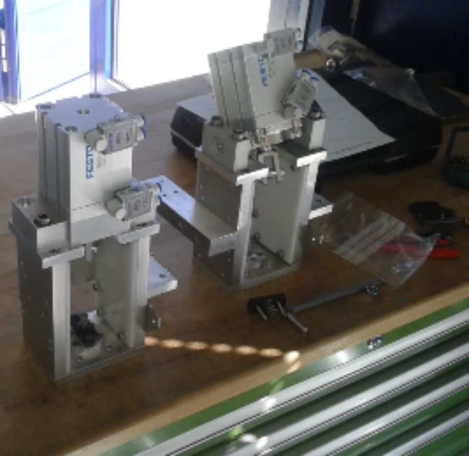 Deux vérins pneumatiques sur un établi avec des outils. Leurs cadres sont argentés et portent le logo Festo.