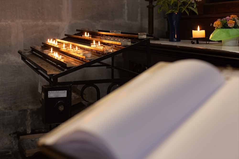 Eine Reihe brennender Kerzen steht auf einem Tisch neben einem offenen Buch.