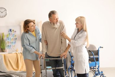 eine Frau hilft einem älteren Mann mit einem Rollator