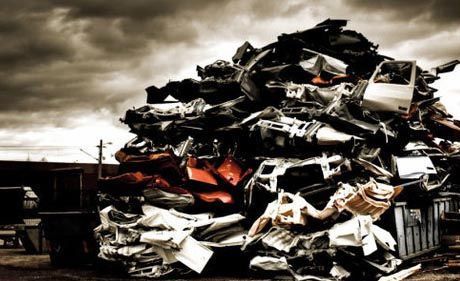 Una gran y caótica pila de chatarra triturada y piezas de automóviles yace bajo un cielo dramático y nublado en un desguace.