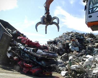 La garra de una grúa hidráulica para chatarra se cierne sobre una gran pila de vehículos aplastados y desechados en un desguace.