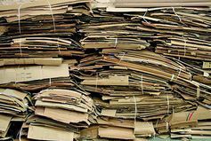 Una pila grande y densa de cajas de cartón aplanadas, atadas con flejes de plástico blanco para su reciclaje.