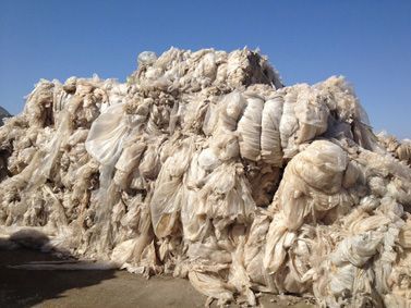 Una gran y desordenada pila de residuos de plástico transparente y envases bajo un cielo azul brillante.