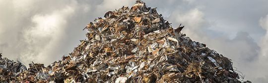 Una enorme y altísima montaña de chatarra y escombros diversos bajo un cielo nublado y cubierto de nubes.