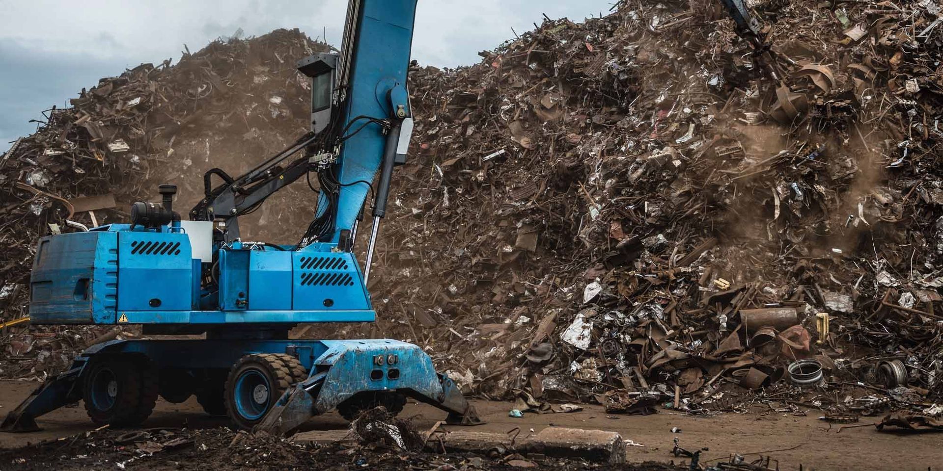 Un operario industrial azul que manipula chatarra trabaja en una gran planta de reciclaje de metales.