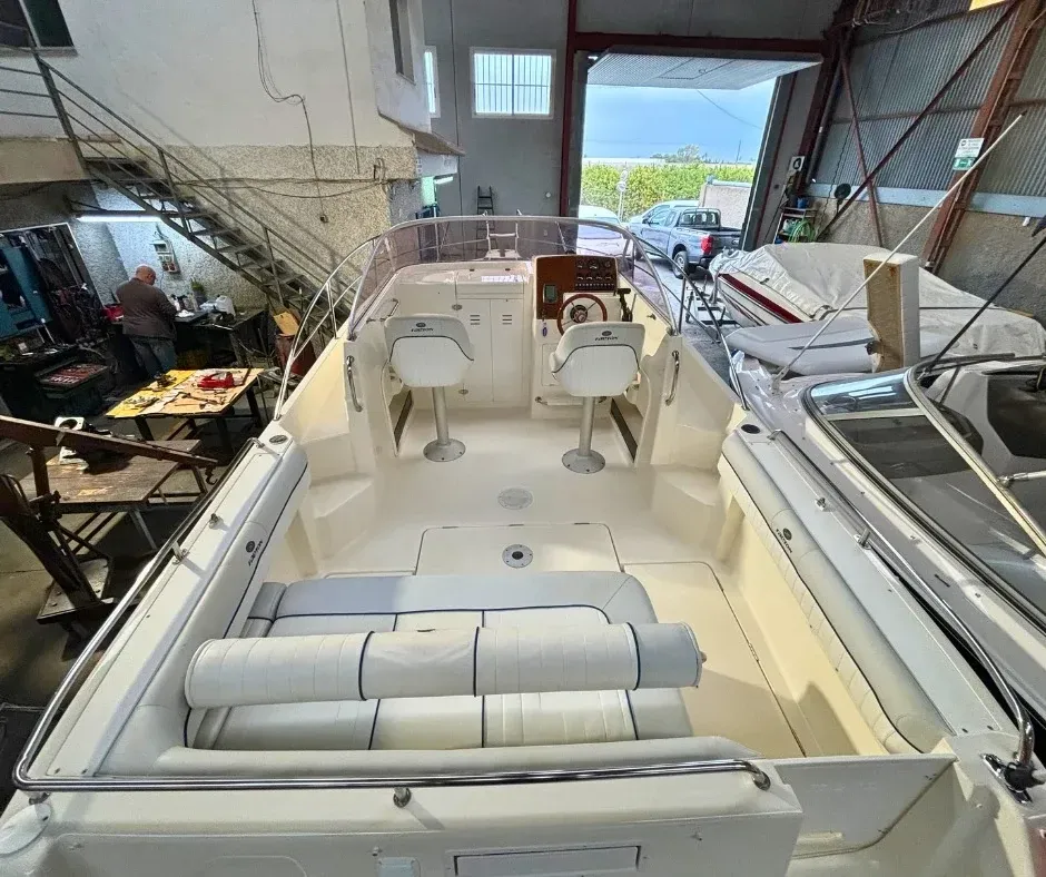 Interior de una embarcación en un taller de reparación, con asientos y volante visibles.