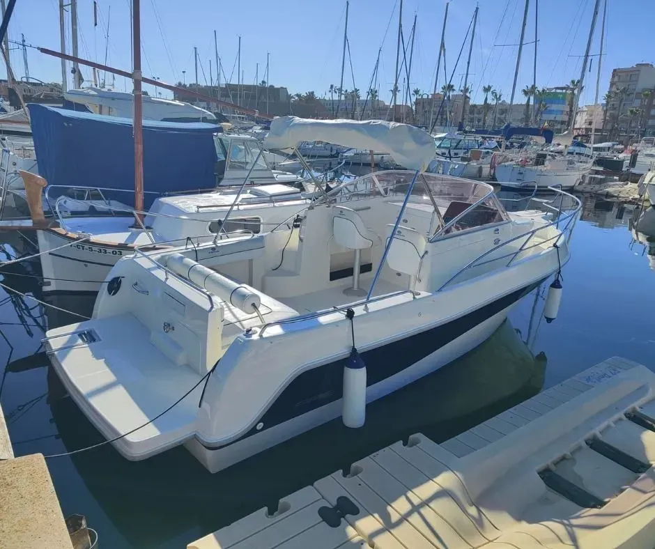Lancha motora blanca con cabina atracada en un puerto deportivo con veleros al fondo.