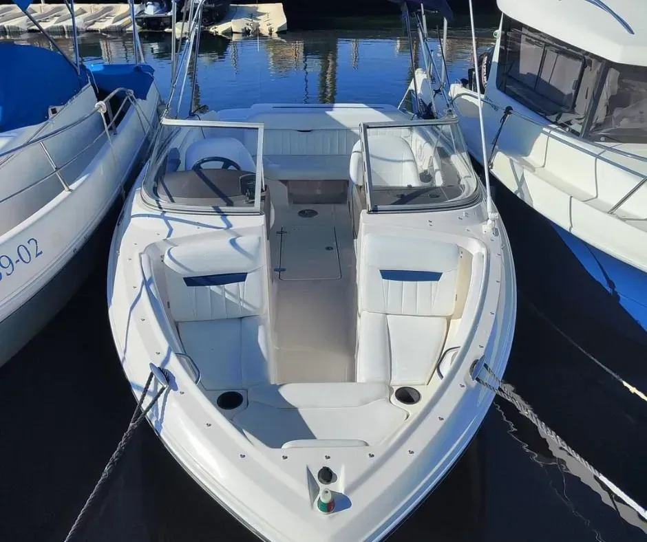 Lancha motora blanca atracada entre barcos más grandes en un puerto deportivo, vista desde arriba.
