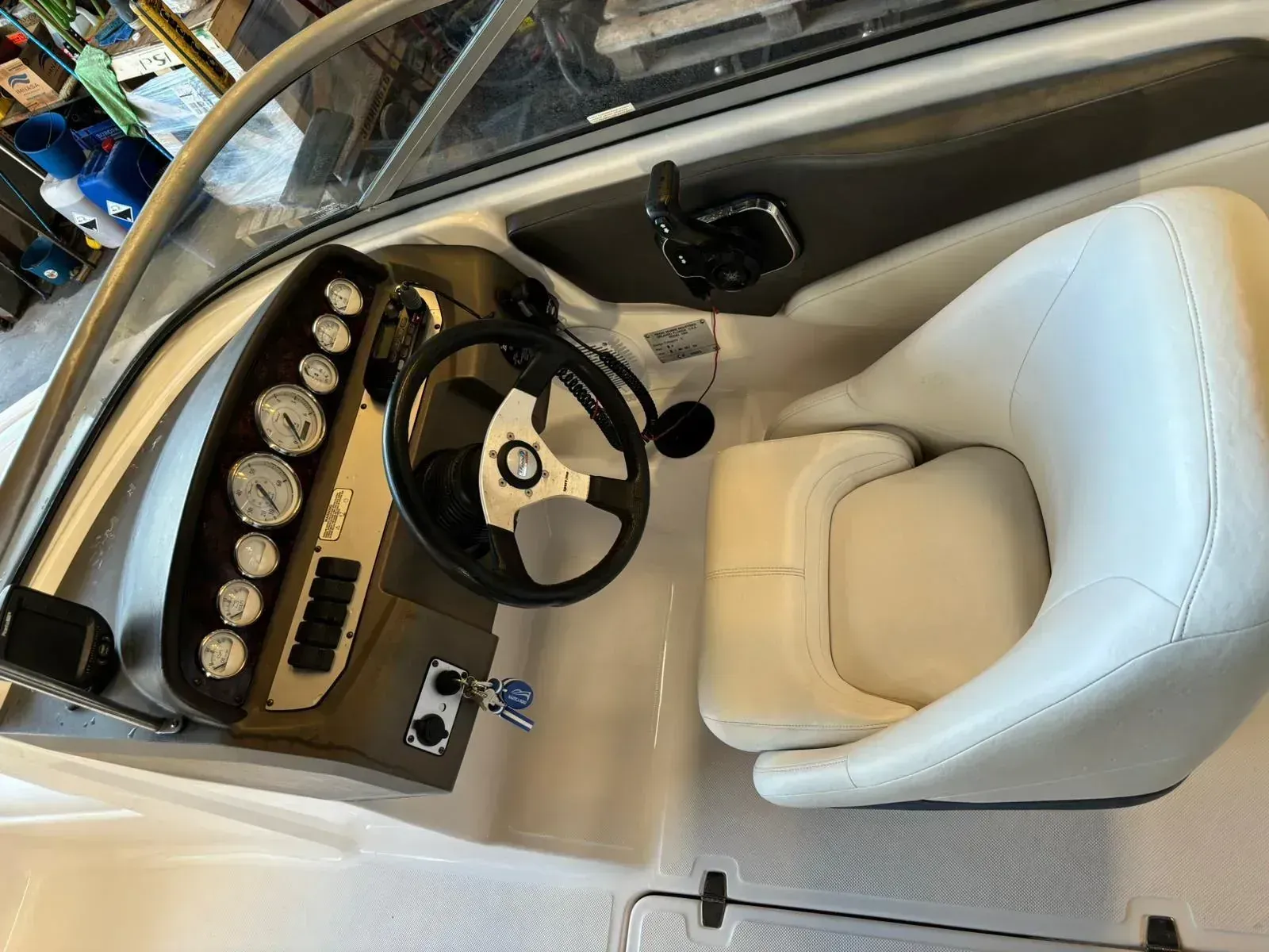 Cabina de barco blanca con volante, indicadores y asiento de capitán color crema; vista desde el muelle.