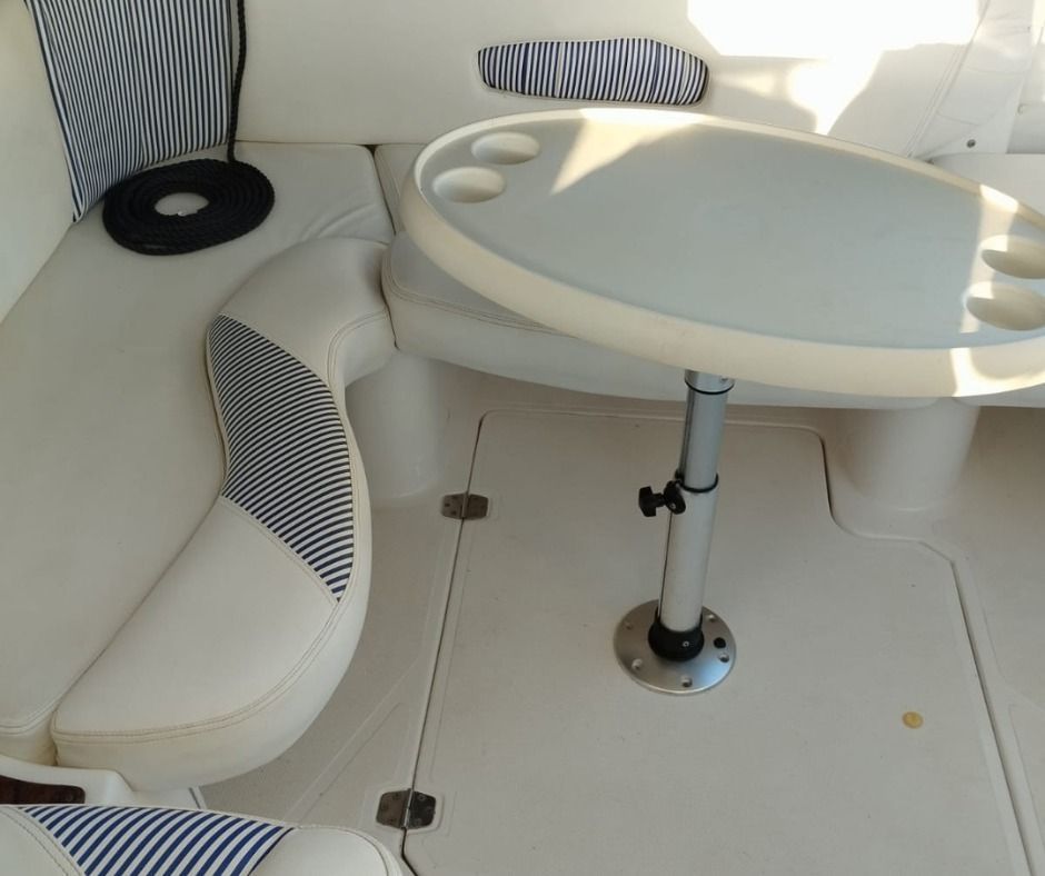 Interior de barco con asientos blancos, detalles de rayas azules y una mesa redonda.