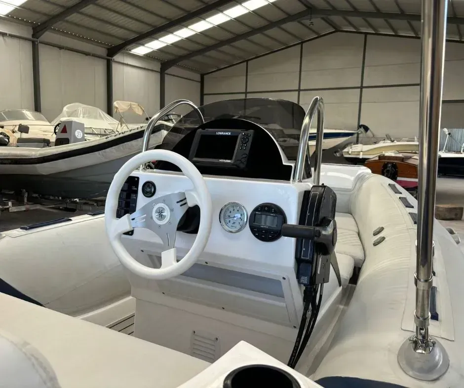 Puesto de mando de barco blanco con volante y medidores dentro de un área de almacenamiento de barcos cubierta.