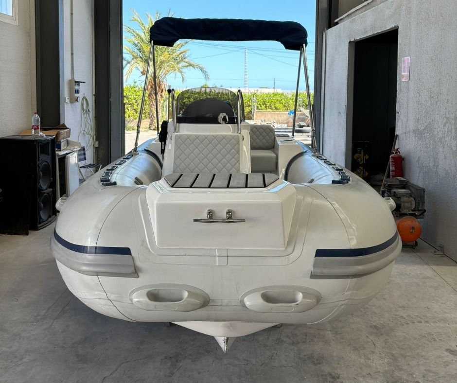 Embarcación neumática rígida de color blanco con detalles en azul, bajo un toldo azul, en un garaje.