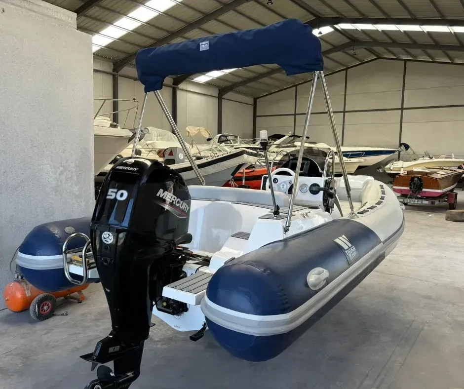 Pequeña lancha motora azul y blanca con toldo y motor fueraborda en un compartimento de almacenamiento cubierto.