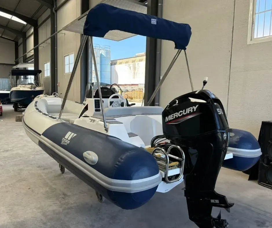 Bote inflable gris con toldo azul y motor fueraborda Mercury dentro de un cobertizo para botes.