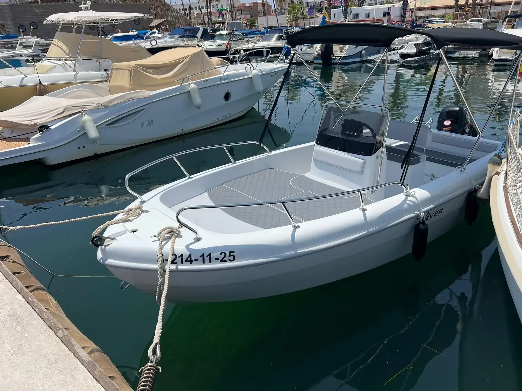 Lancha motora blanca con cubierta negra atracada en un puerto deportivo, otras embarcaciones al fondo.